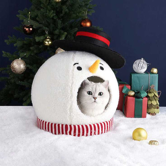 Snowman Cat Covered Bed with white cat inside, placed on snow with Christmas tree and gifts, ideal for festive pet comfort.