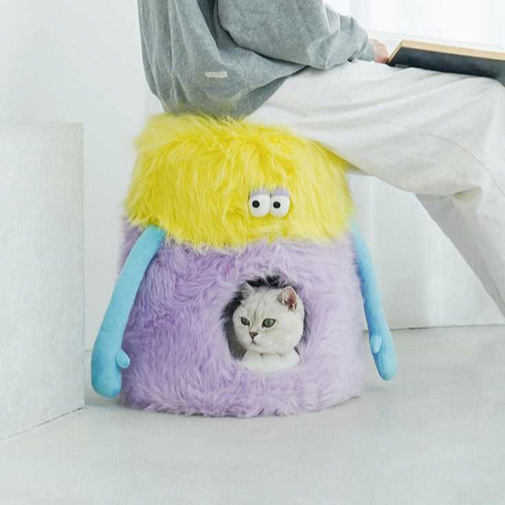 Person sitting on the Little Monster Stool Cat Bed while a cat rests inside, showing dual function as a seat and pet bed.