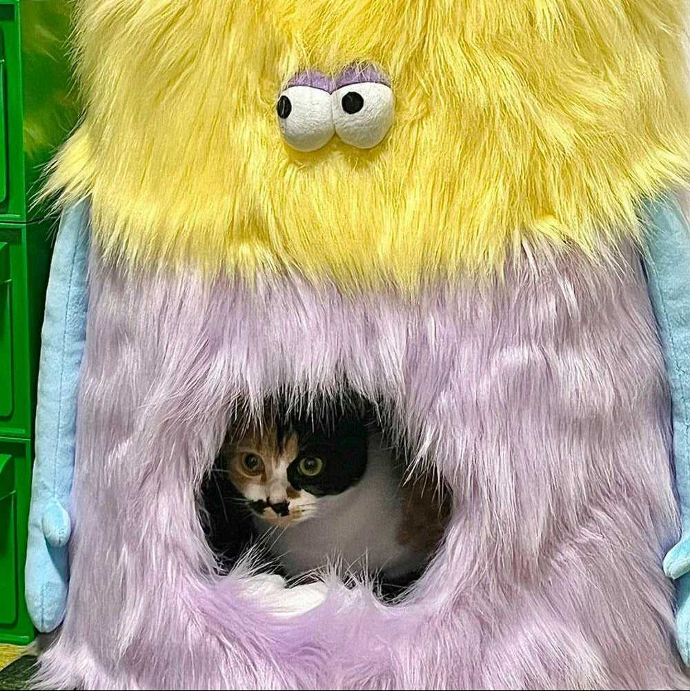 Black and white cat inside the Little Monster Stool Cat Bed, peeking through the circular entrance of the plush monster.
