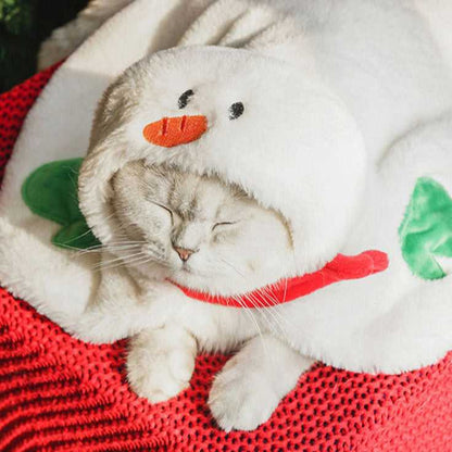 White cat wearing snowman-themed costume with carrot nose hood from Gift Set Cat Christmas Costumes, lying on red blanket.
