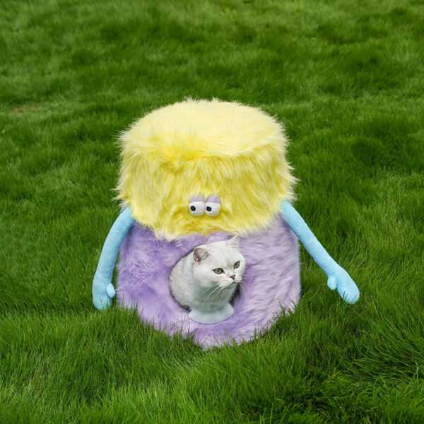 Little Monster Stool Cat Bed on green grass with a cat peeking out. Plush and playful cat furniture for indoor or outdoor use.