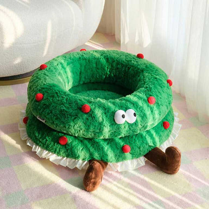 Christmas Wreath Shaped Cat Bed in sunlight, highlighting its fluffy green build, red dots, and whimsical cartoon eyes.
