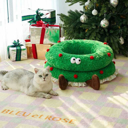 Cat lounging beside the Christmas Wreath Shaped Cat Bed near a Christmas tree, ideal for holiday-themed pet furniture.