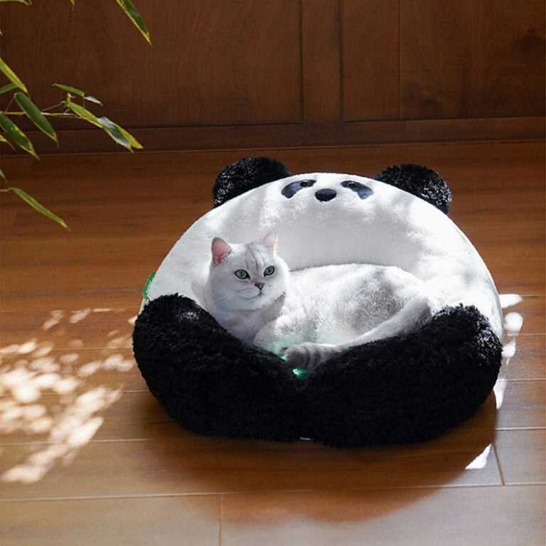 White cat resting in the Panda Hug Cat Bed on a wooden floor, highlighting the cozy panda design and soft green cushion.