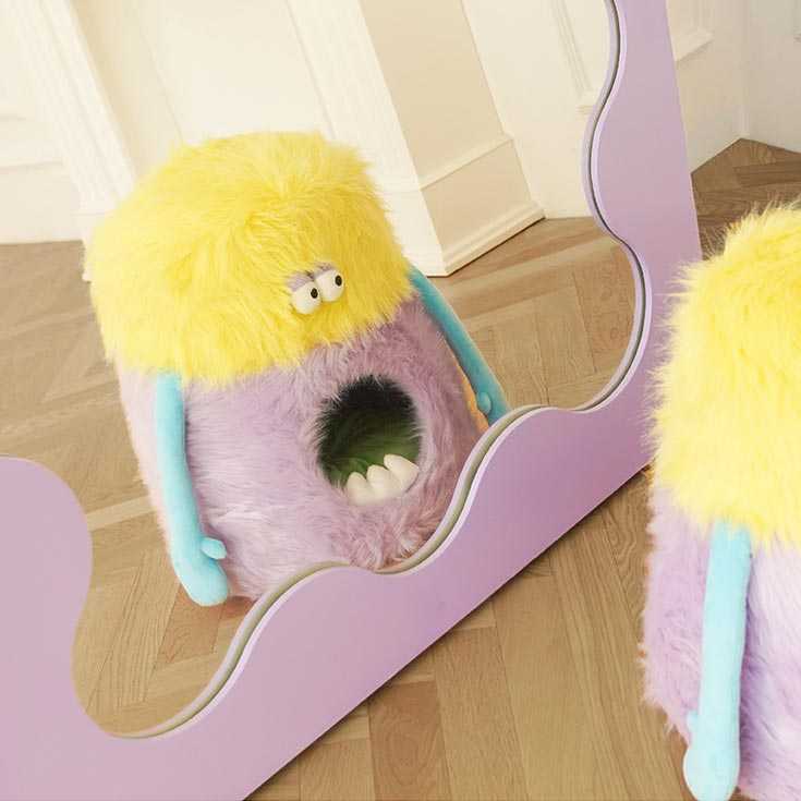 Little Monster Stool Cat Bed looking into a mirror, showcasing its monster face and soft plush texture for stylish cat lounging.