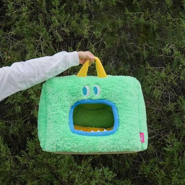 Green Monster Series Cat Bed with monster face and yellow handle held outdoors, highlighting its portable and fun design.