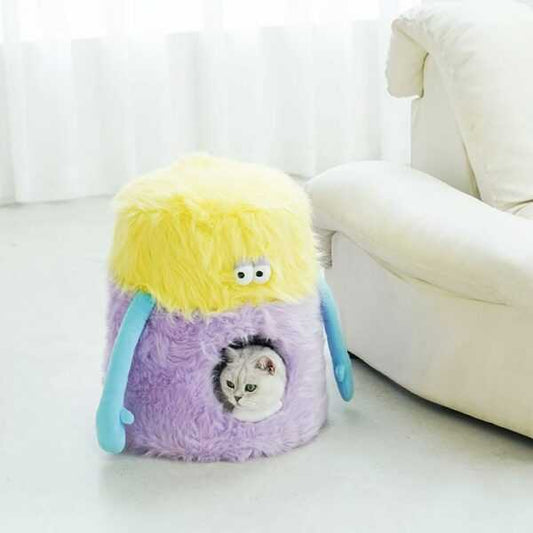 Little Monster Stool Cat Bed in pastel yellow and purple with a cat inside, placed beside a white sofa. Fun cat furniture for cozy lounging.