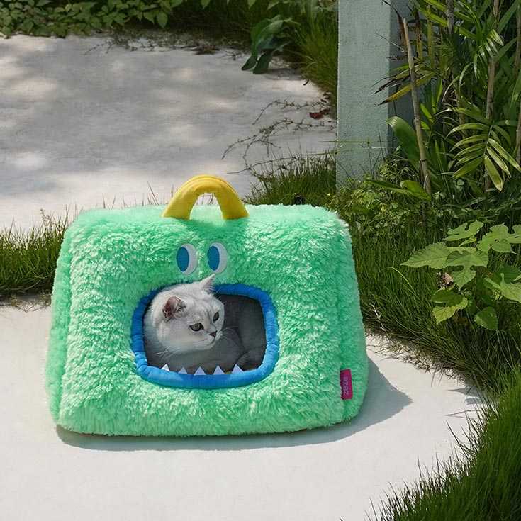White cat resting inside green Monster Series Cat Bed with monster face, perfect for cozy indoor or outdoor cat lounging.